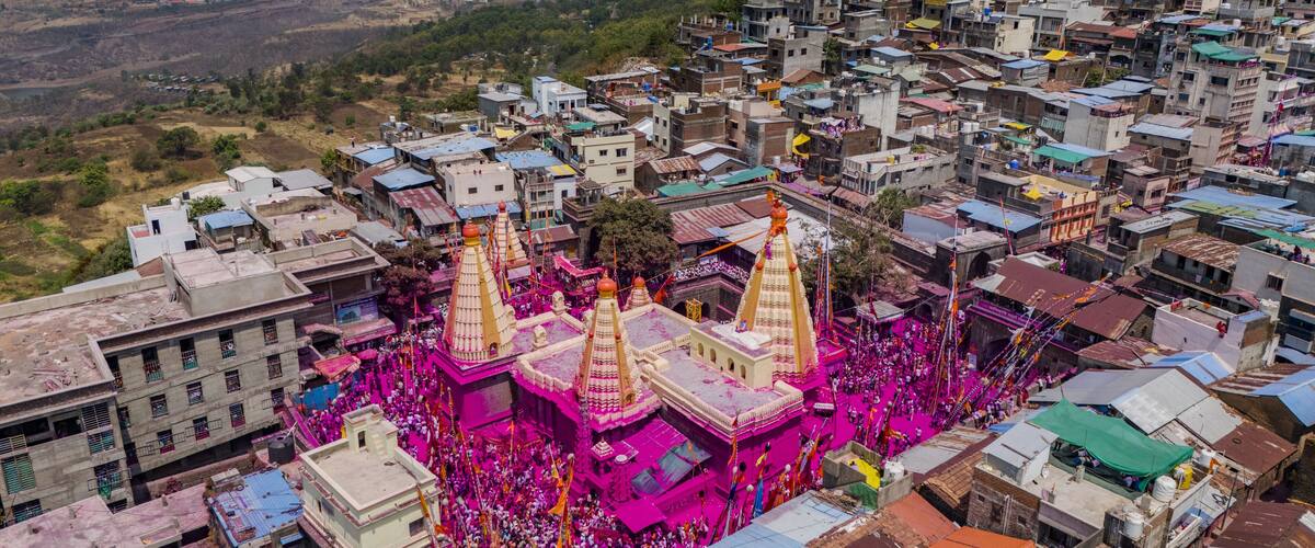 Aerial view of the vibrant pink-hued Jyotiba Temple amidst a sea of devotees and colorful decorations, nestled within a densely packed urban landscape, Jyotiba Dongar, Maharashtra, India.