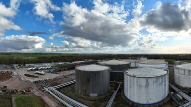 Aerial view of cylindrical oil tanks gleaming under the expansive sky contrast against the lush green fields, Kingsbury Oil Terminal, Tamworth, United Kingdom.