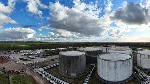 Aerial view of cylindrical oil tanks gleaming under the expansive sky contrast against the lush green fields, Kingsbury Oil Terminal, Tamworth, United Kingdom.