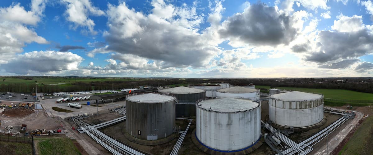 A large industrial facility with multiple cylindrical storage tanks, surrounded by a fenced area and a road.