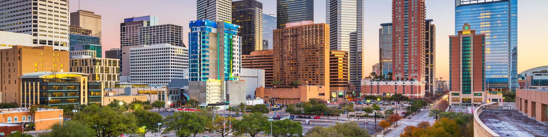 A city skyline with modern skyscrapers, a busy street with cars, and trees lining the roads.