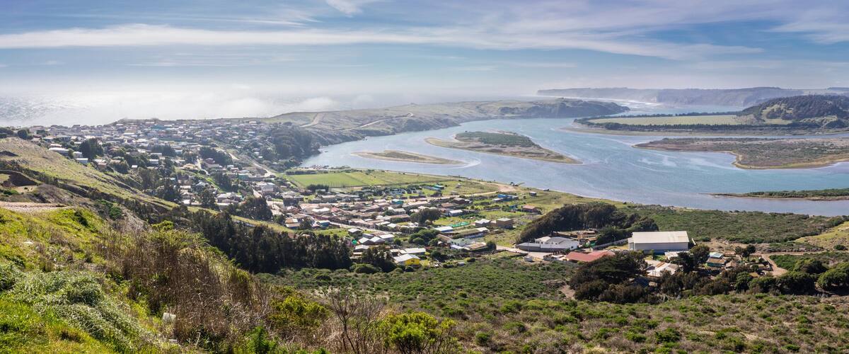 A coastal town with a river delta, green hills, and a clear sky.