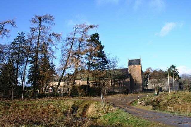 A stone building with a tower, surrounded by trees and a dirt path.