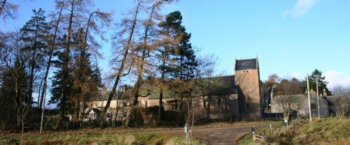 A stone building with a tower, surrounded by trees and a dirt path.