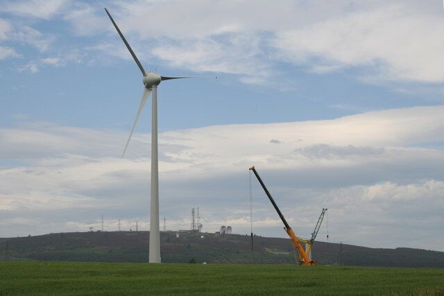 A wind turbine and a crane in a field with a cloudy sky.