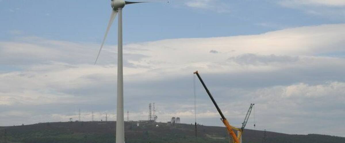 A wind turbine and a crane in a field with a cloudy sky.