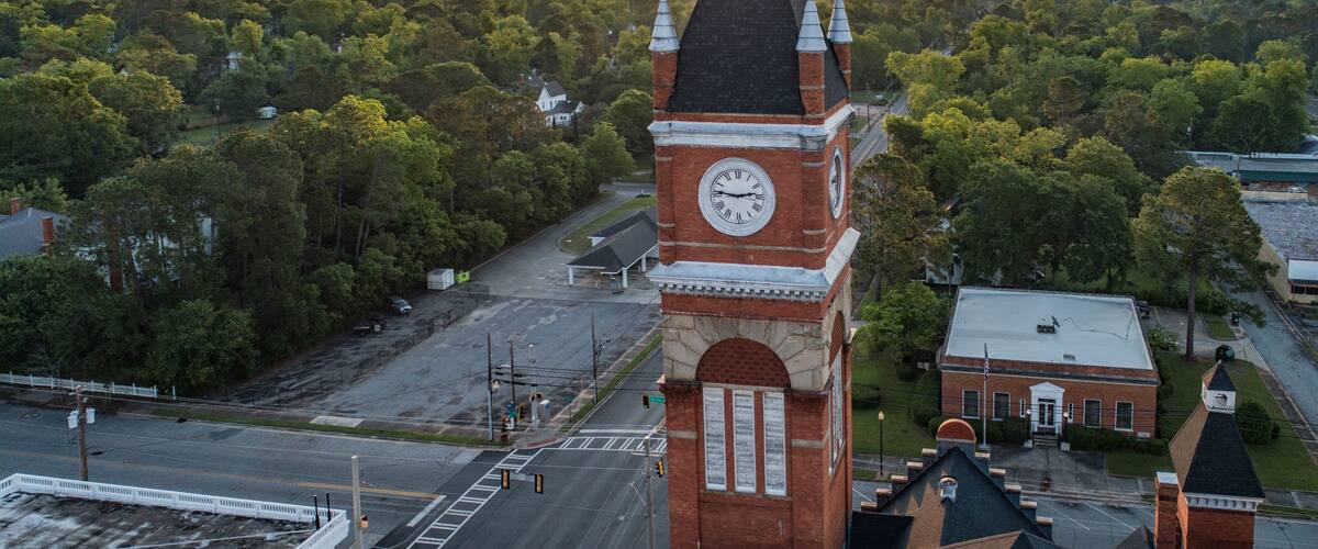 A clock tower with Roman numerals, surrounded by trees and a sunset in the background.