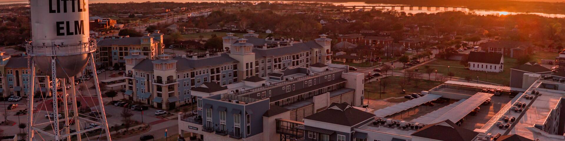 Aerial view of the Little Elm water tower standing tall against a fiery sunset casting a warm glow over the buildings, Little Elm, Texas, United States.