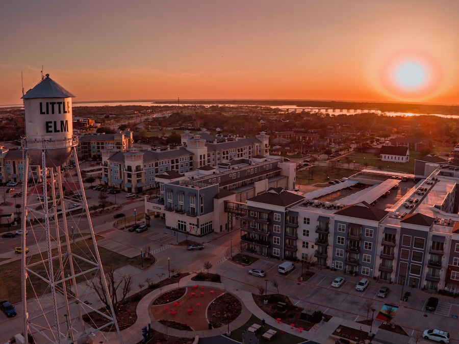 Aerial view of the Little Elm water tower standing tall against a fiery sunset casting a warm glow over the buildings, Little Elm, Texas, United States.