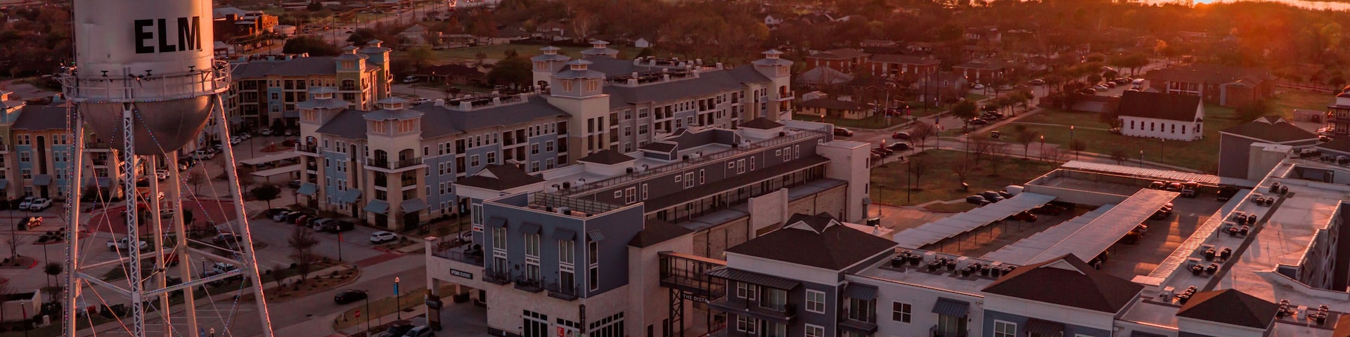 Aerial view of the Little Elm water tower standing tall against a fiery sunset casting a warm glow over the buildings, Little Elm, Texas, United States.