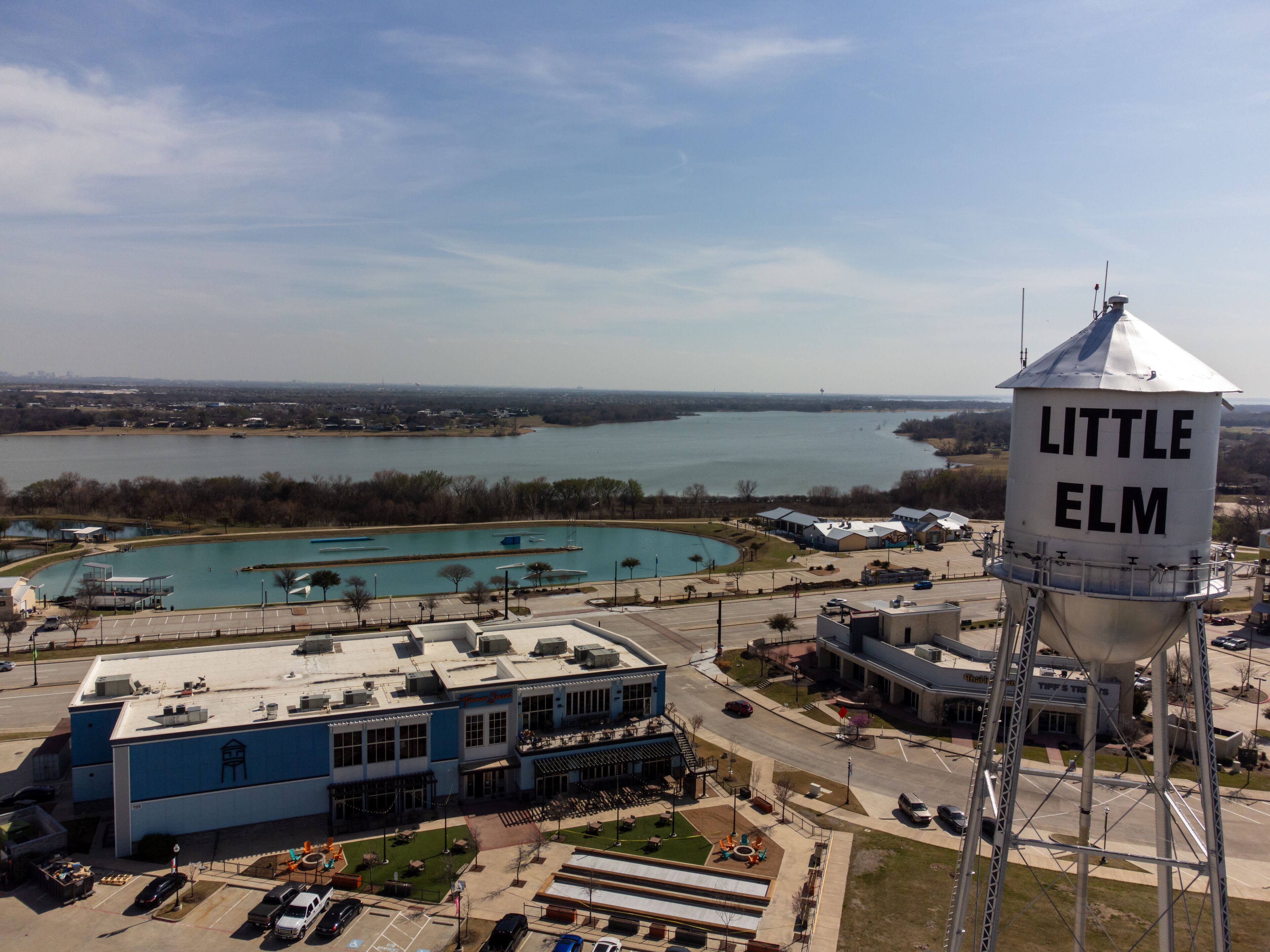 Aerial view of a water tower standing tall against the backdrop of a serene lake, with buildings nestled along the shore, Little Elm, Texas, United States.