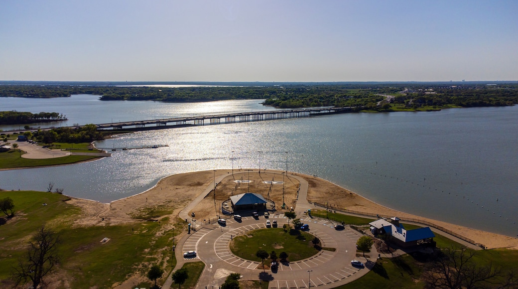 Aerial view of a sun-kissed beach meeting the vast lake under a clear sky, with a bridge stretching across the water, Little Elm, Texas, United States.
