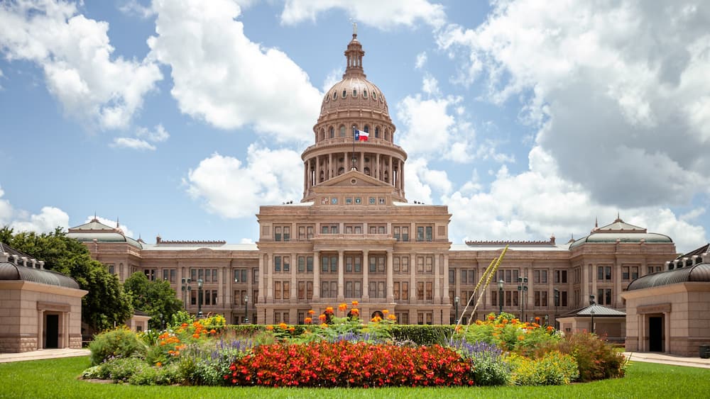 Texas State Capitol in Austin, Texas on a sunny summer day with colorful flowers in the front yard