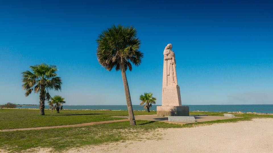 A statue on a pedestal, palm trees, and a clear blue sky.