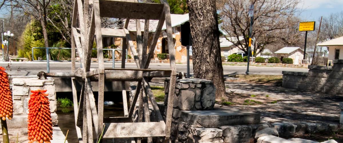 A wooden water wheel, a stone wall, and red flowers in a park.