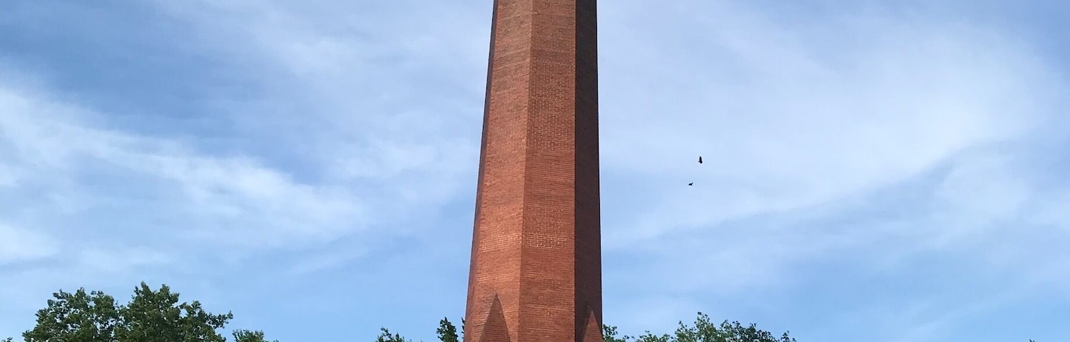 A tall brick monument with a plaque titled "Evolution of an Oil Company" in a grassy field with trees in the background.