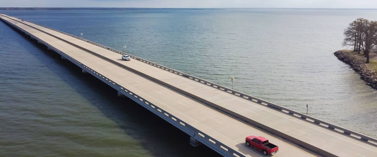 A long bridge over a calm body of water with a red truck on the right side.