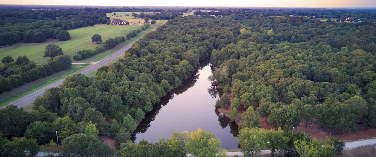 A river winding through a densely wooded area with a road running alongside it.