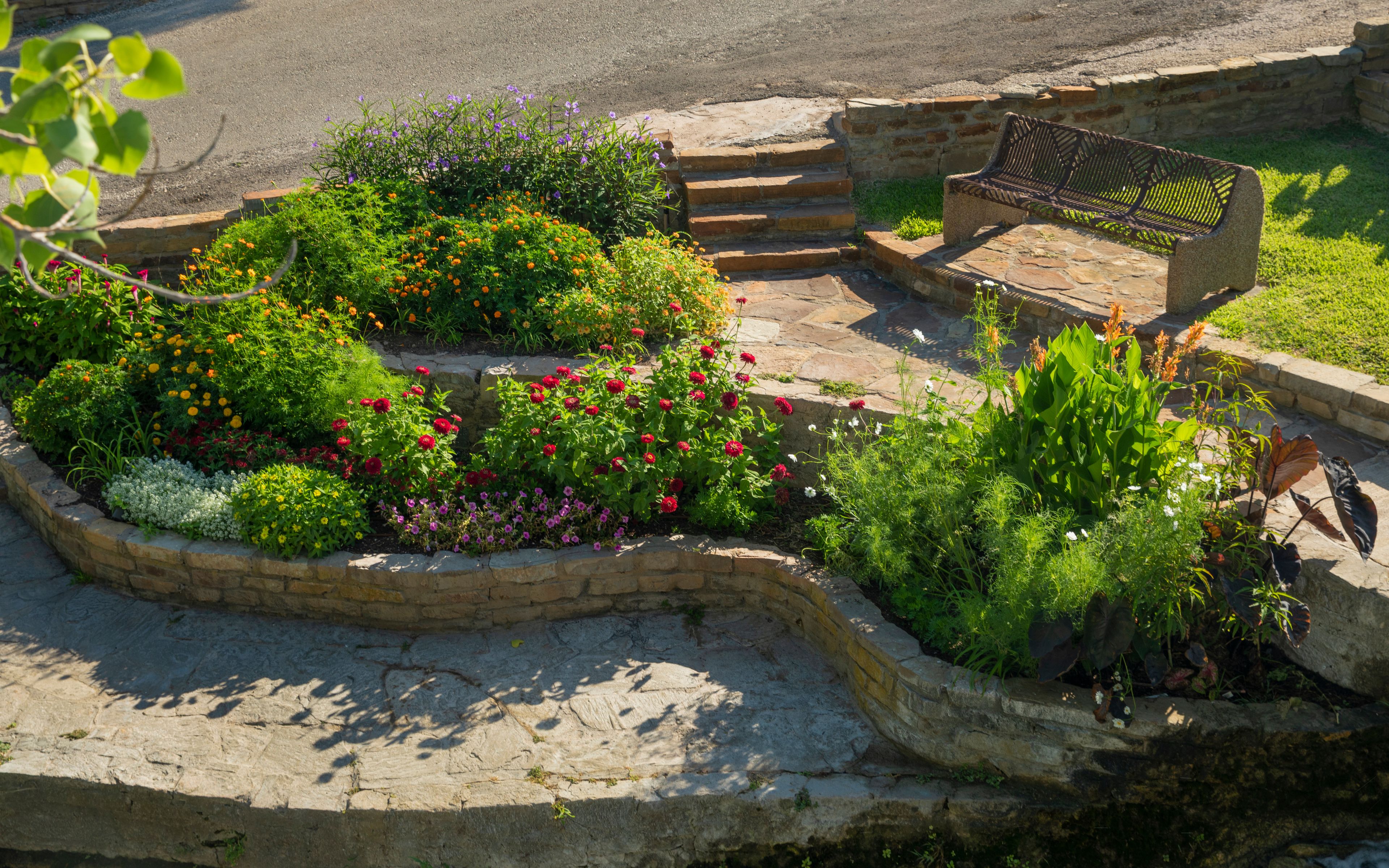 A landscaped garden with a variety of colorful flowers, a stone bench, and a stone pathway.