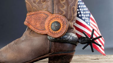 A cowboy boot with a decorative belt and a flag.