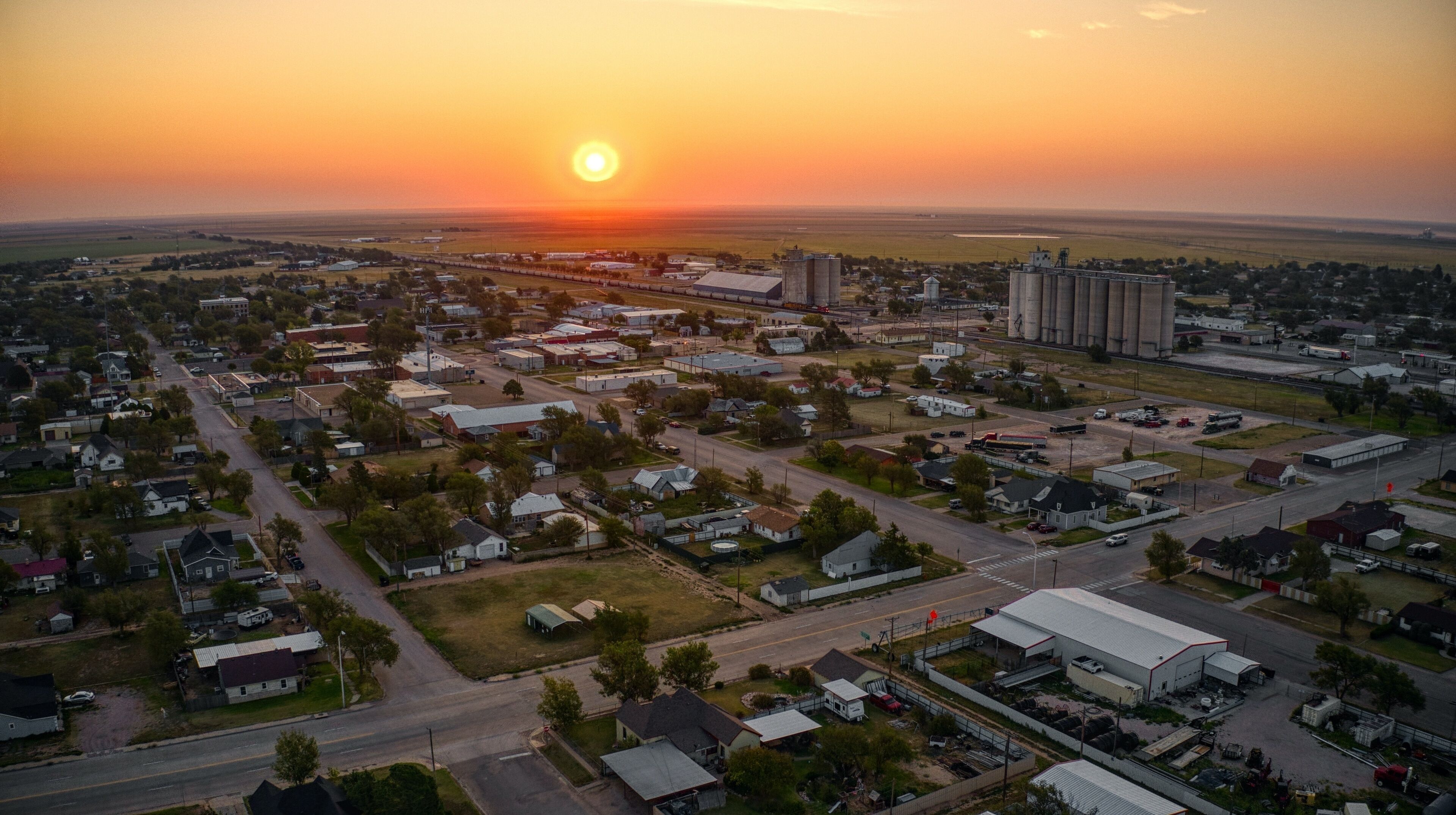 A town at sunset with a prominent grain silo and a large industrial building.