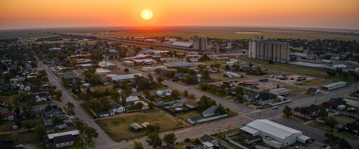 A town at sunset with a prominent grain silo and a large industrial building.