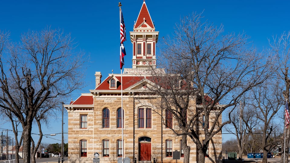 A historic stone building with a red roof and a steeple, surrounded by leafless trees.