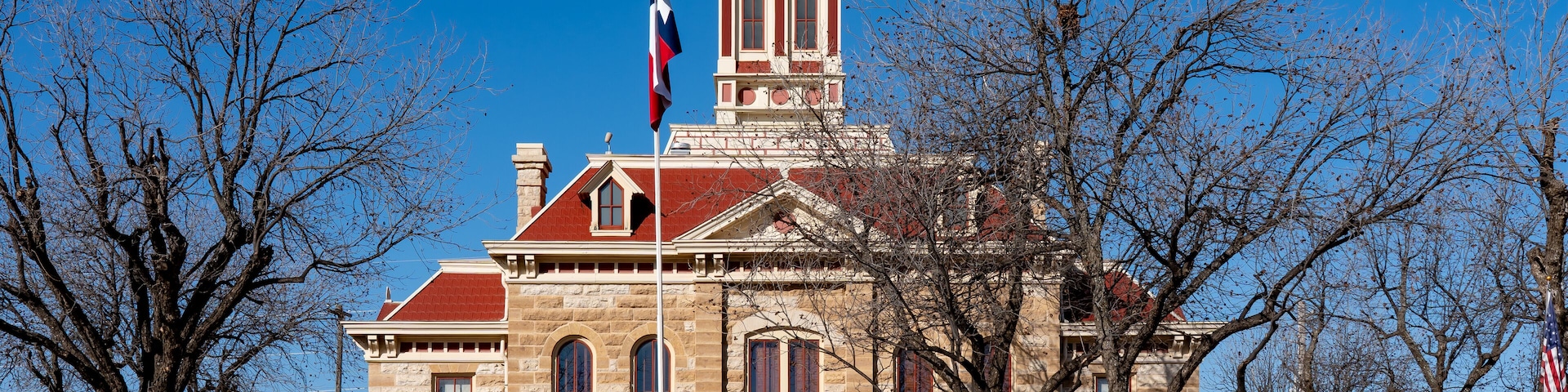 A historic stone building with a red roof and a steeple, surrounded by leafless trees.