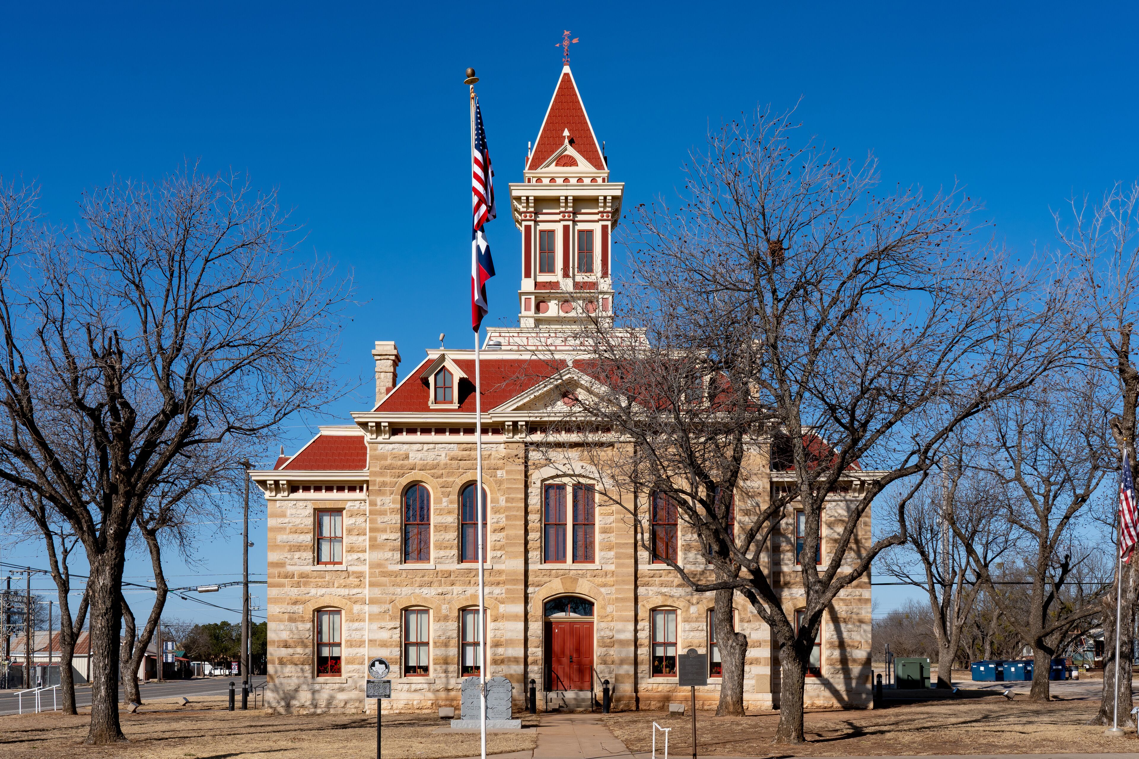 A historic stone building with a red roof and a steeple, surrounded by leafless trees.