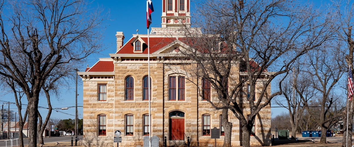 A historic stone building with a red roof and a steeple, surrounded by leafless trees.