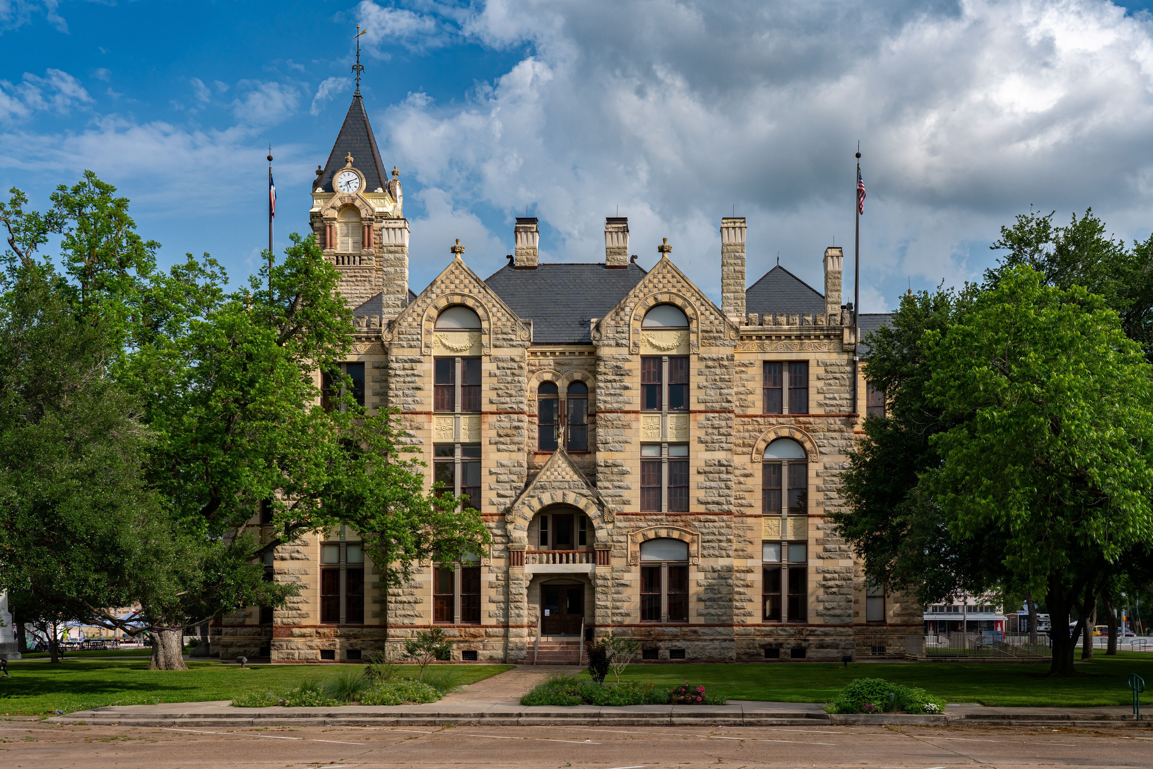 A historic stone building with a clock tower, arched windows, and a flagpole.