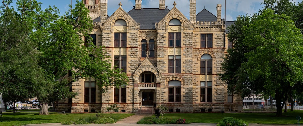 A historic stone building with a clock tower, arched windows, and a flagpole.