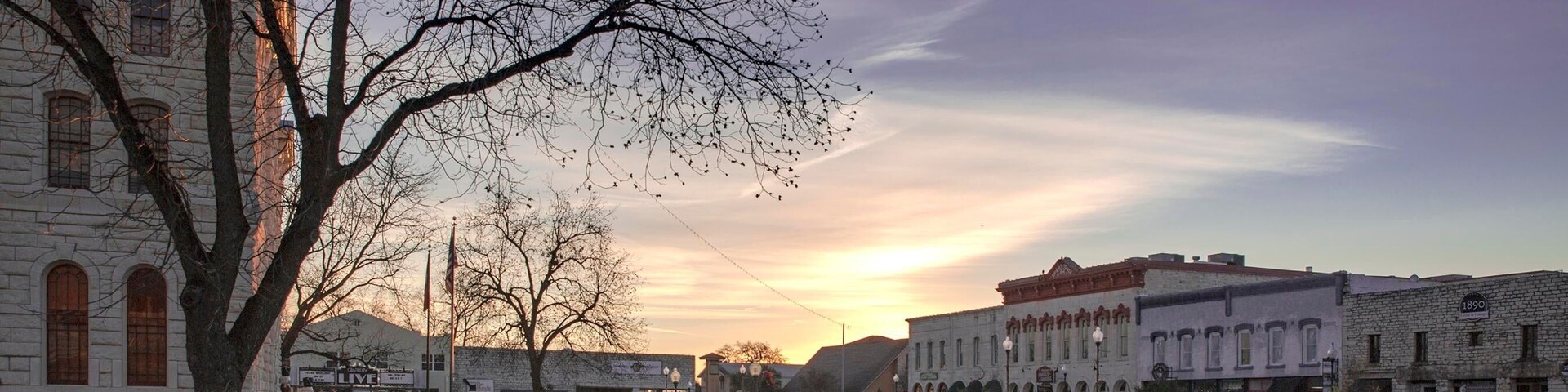 Rua histórica no centro da cidade, com edifícios, uma árvore e um pôr do sol.