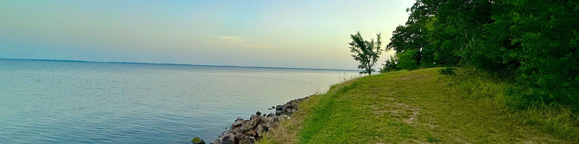A calm lake with a rocky shoreline and grassy banks.