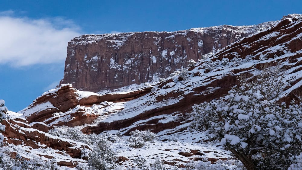 A snow-covered mountain with a prominent rock face and trees in the foreground.