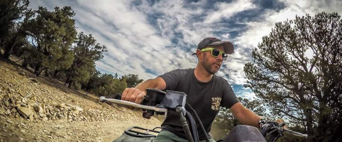 A person riding an ATV on a dirt path with trees and a cloudy sky in the background.