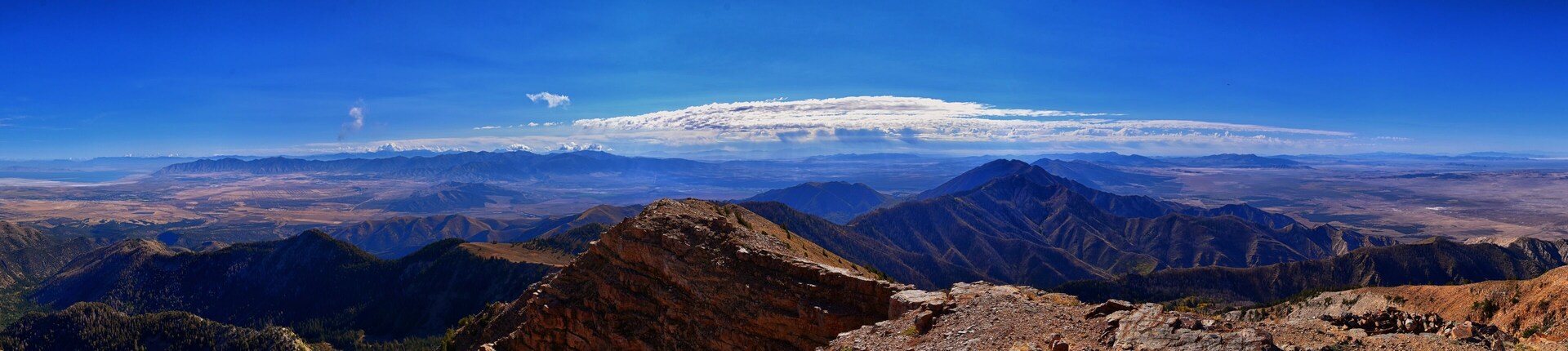 Una cordillera con un pico nevado a lo lejos, terreno rocoso en primer plano y un cielo azul despejado.