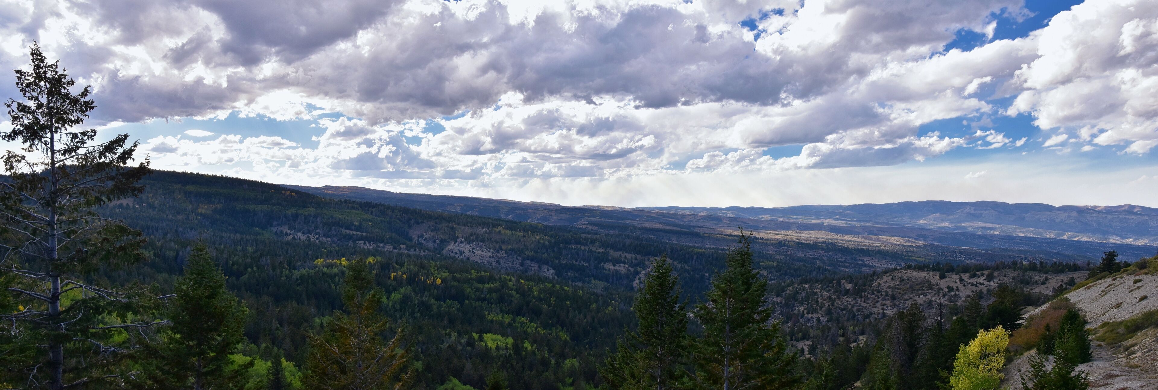 A mountainous landscape with dense forests and a partly cloudy sky.