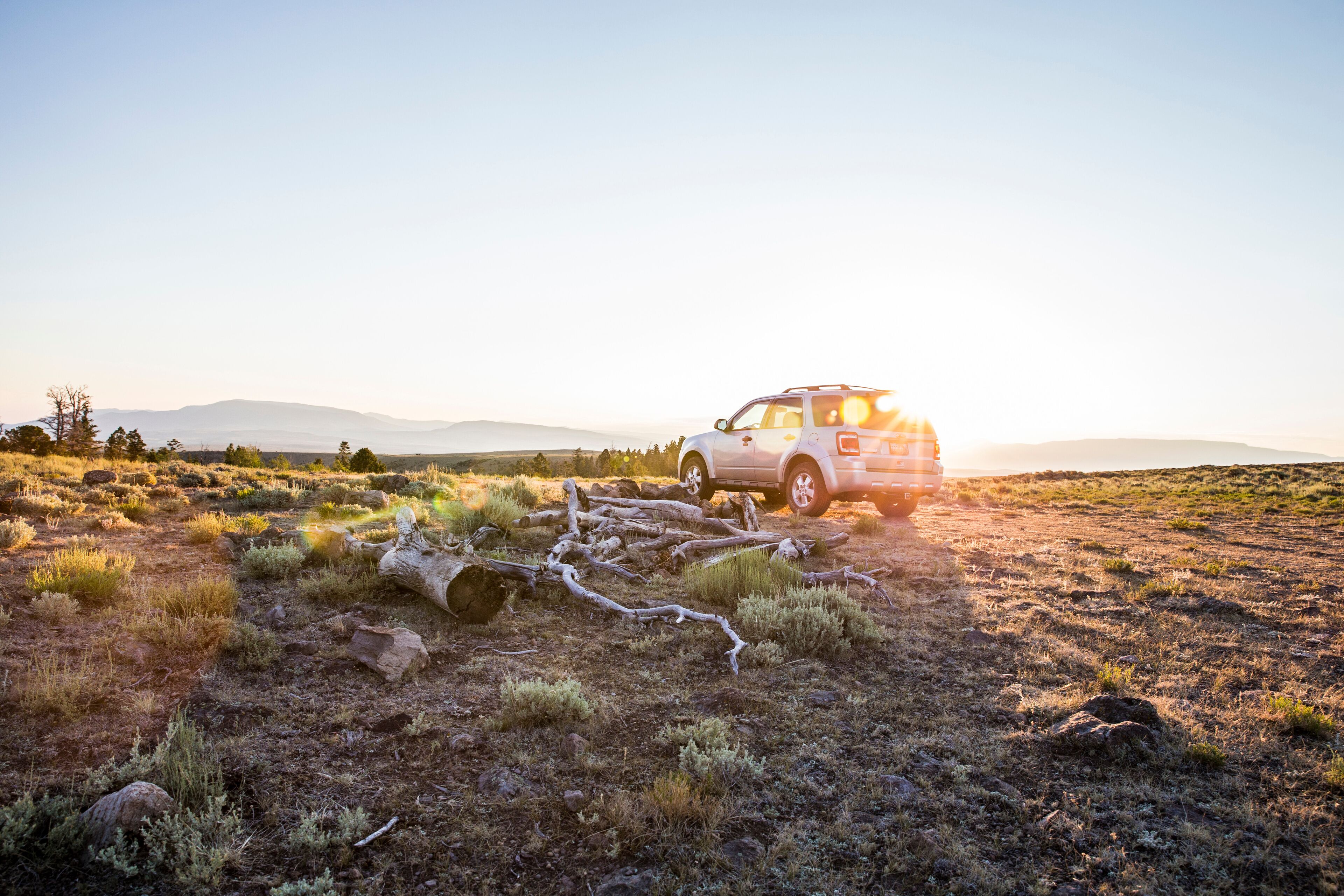 A white SUV on a dirt road in a dry, grassy field with scattered rocks and a clear sky.