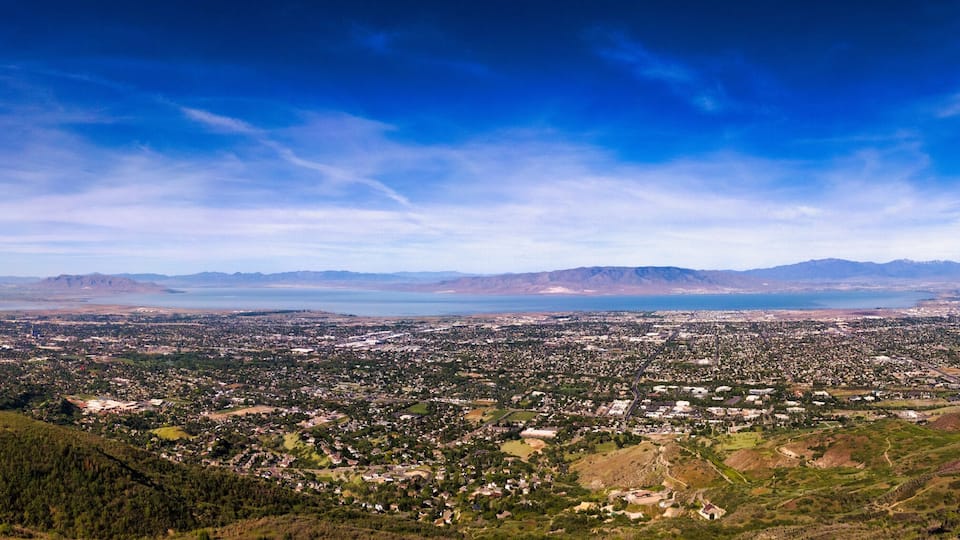 A panoramic view of a valley with a city, mountains, and a large body of water.