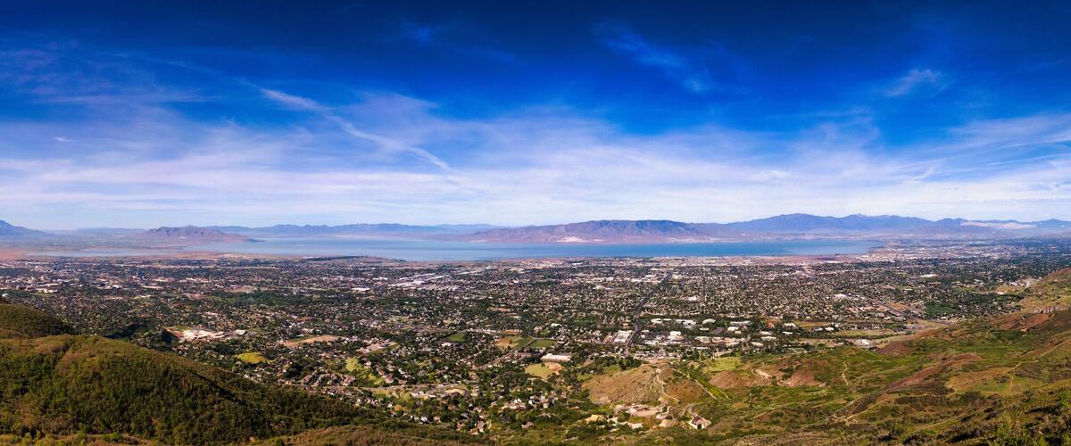 A panoramic view of a valley with a city, mountains, and a large body of water.