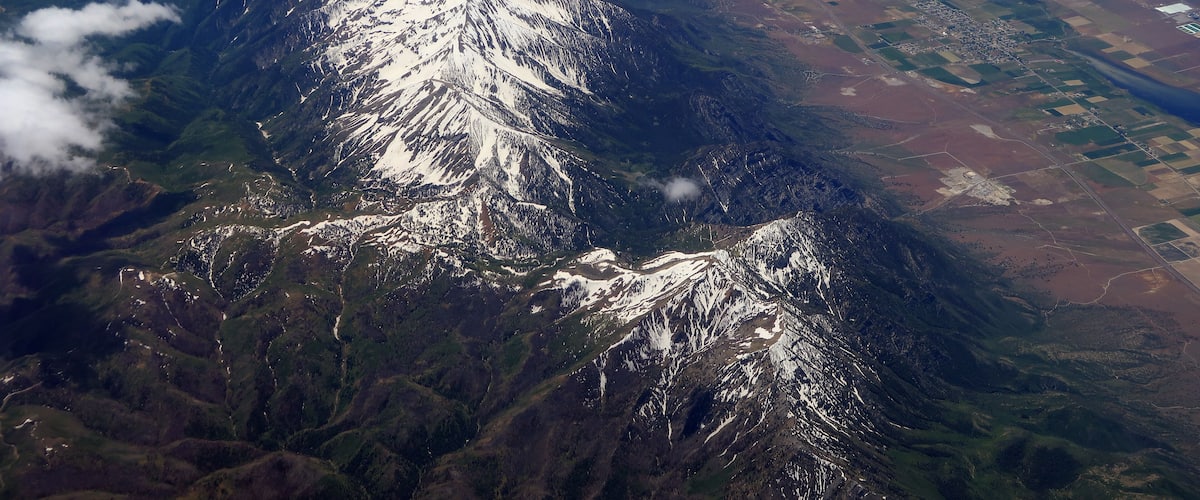 A snow-capped mountain range with a river and agricultural fields.