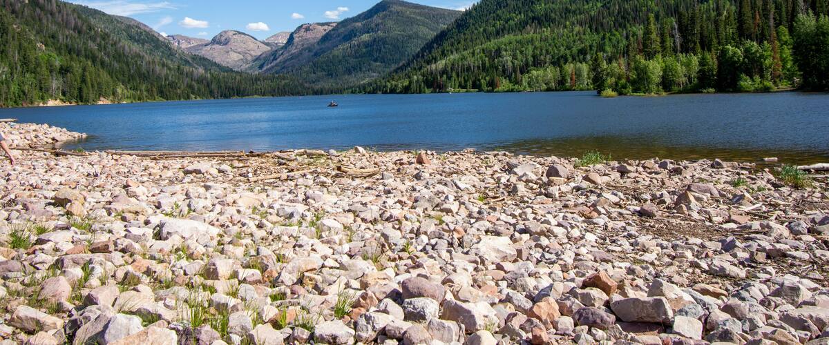 A rocky shoreline with a lake surrounded by forested mountains.
