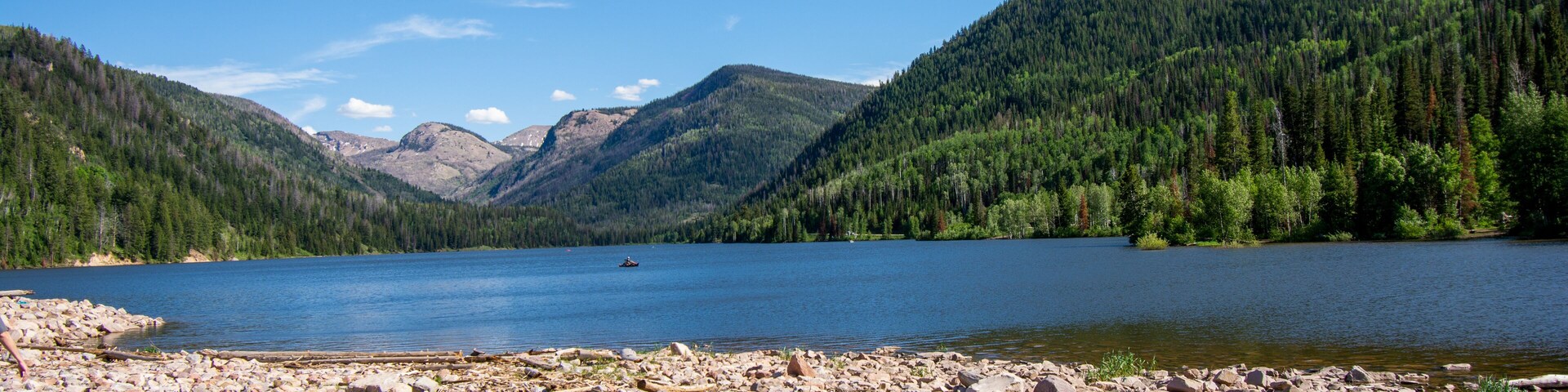 A rocky shoreline with a lake surrounded by forested mountains.