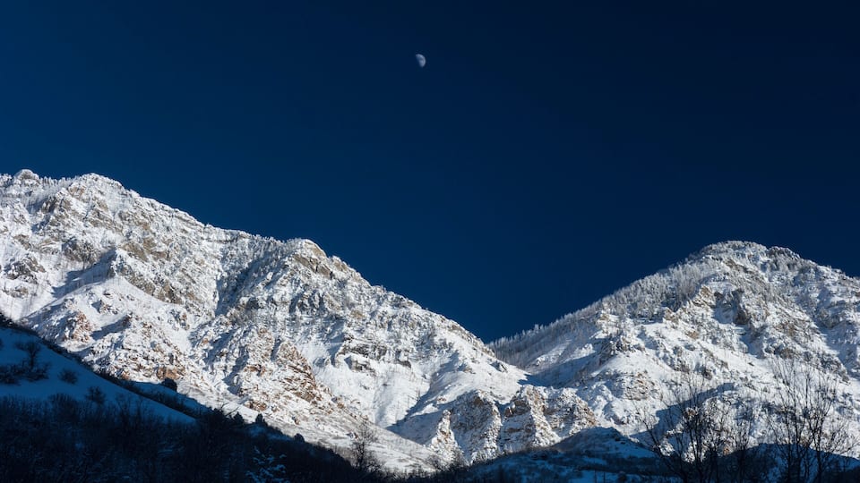 A snow-covered mountain range with a crescent moon in the sky.