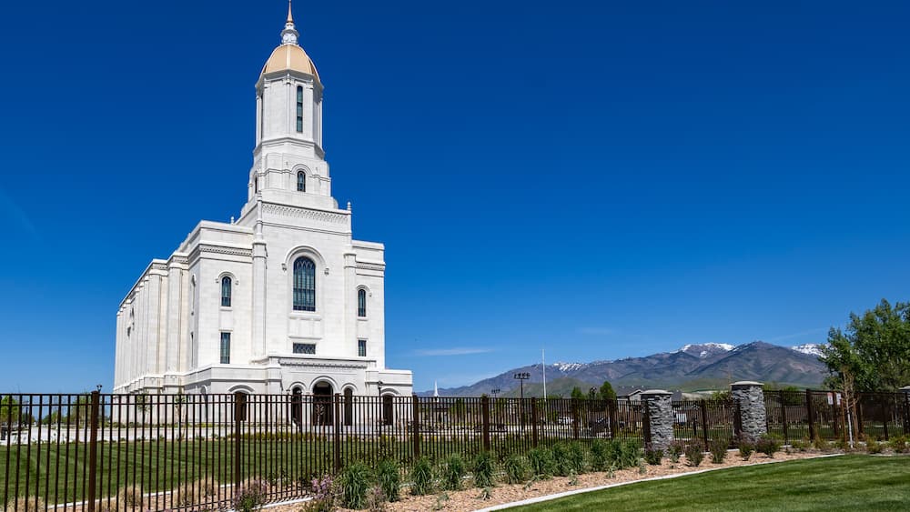 A white church with a tall steeple and a mountain range in the background.