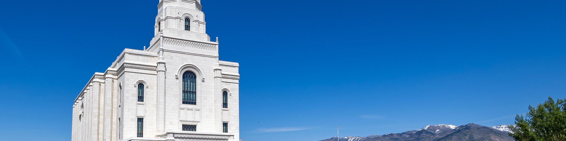 Una iglesia blanca con un campanario alto y una cadena montañosa al fondo.