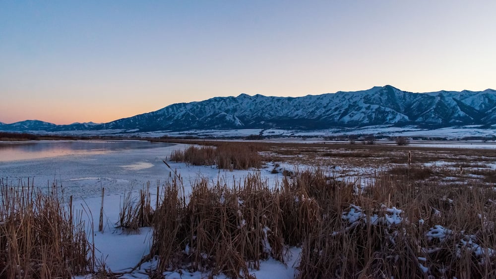 A frozen lake with snow-covered mountains in the background.