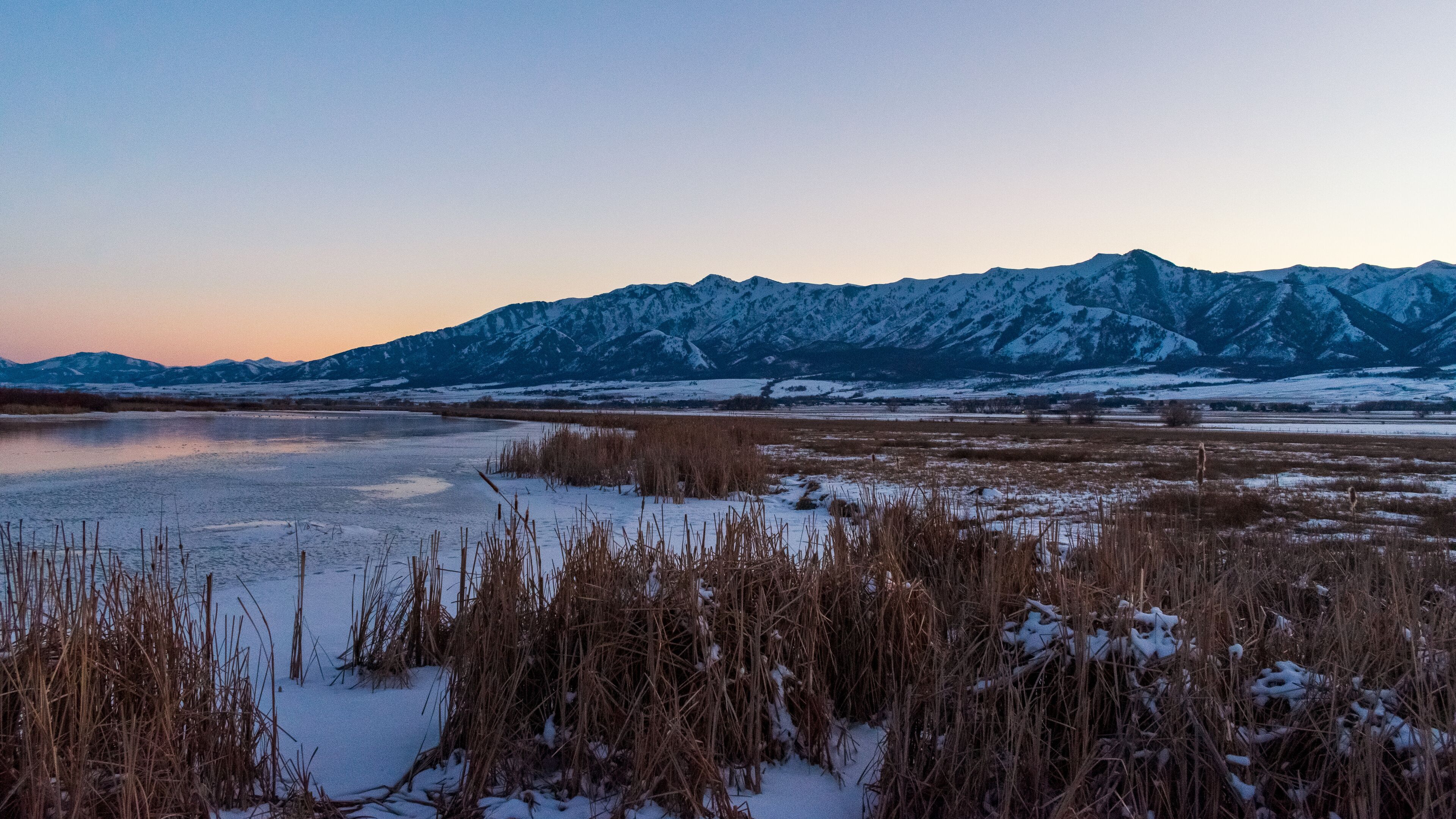 A frozen lake with snow-covered mountains in the background.