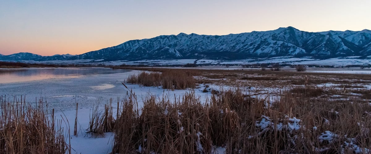 A frozen lake with snow-covered mountains in the background.